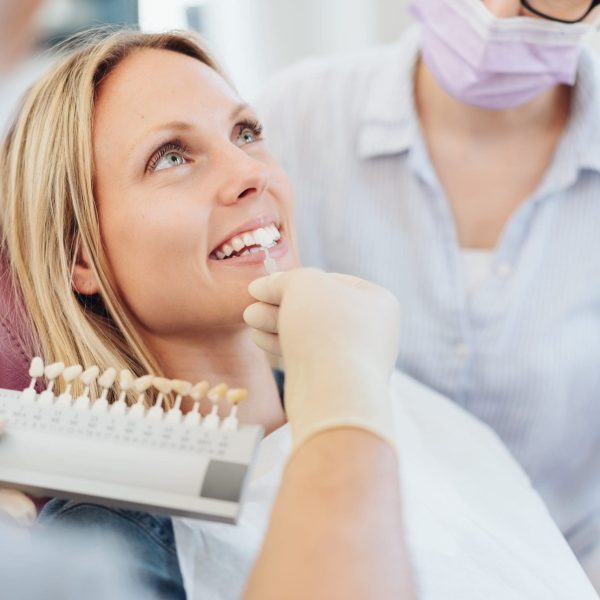 Dentist checking the whiteness of a patients teeth against color coded samples during an examination in his surgery